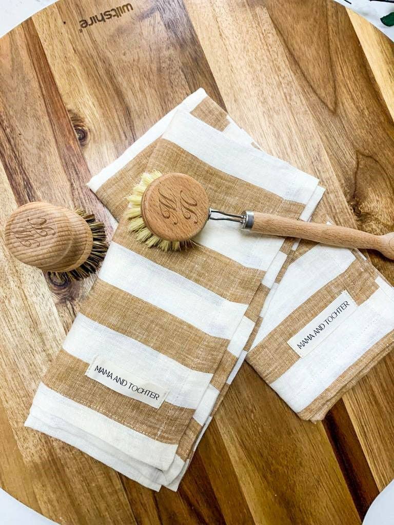 Set of cleaning tools including a wooden scrubber, brush, and tea towels on a wooden surface.
