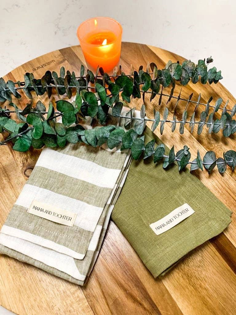 Two green napkins with striped pattern on a wooden surface with a candle and eucalyptus leaves.