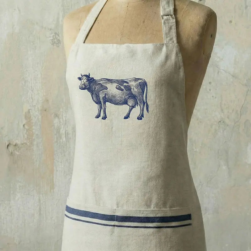 Beige apron with a cow print on a wooden mannequin against a textured beige background