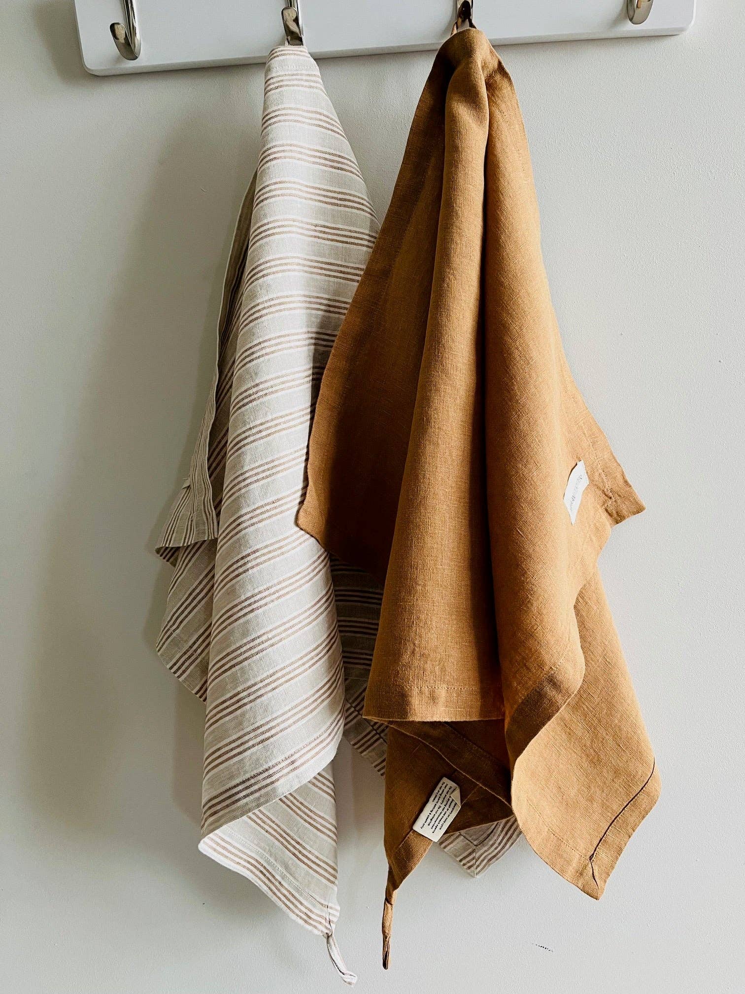 Two towels, one beige and one brown, hanging on a white hook against a white wall.