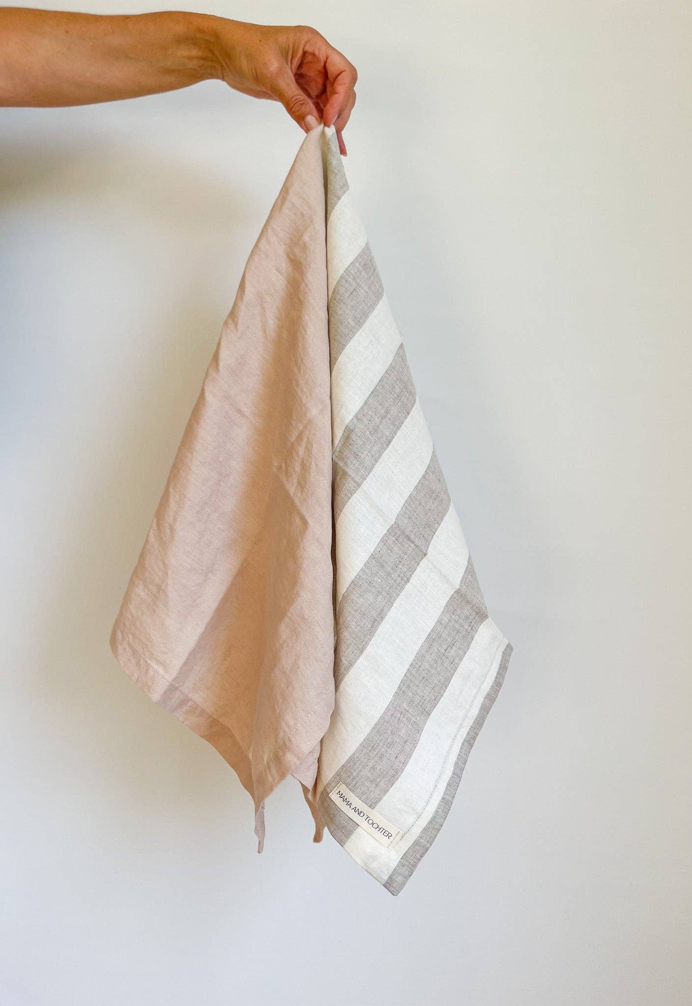 Hand holding two striped towels against a plain background