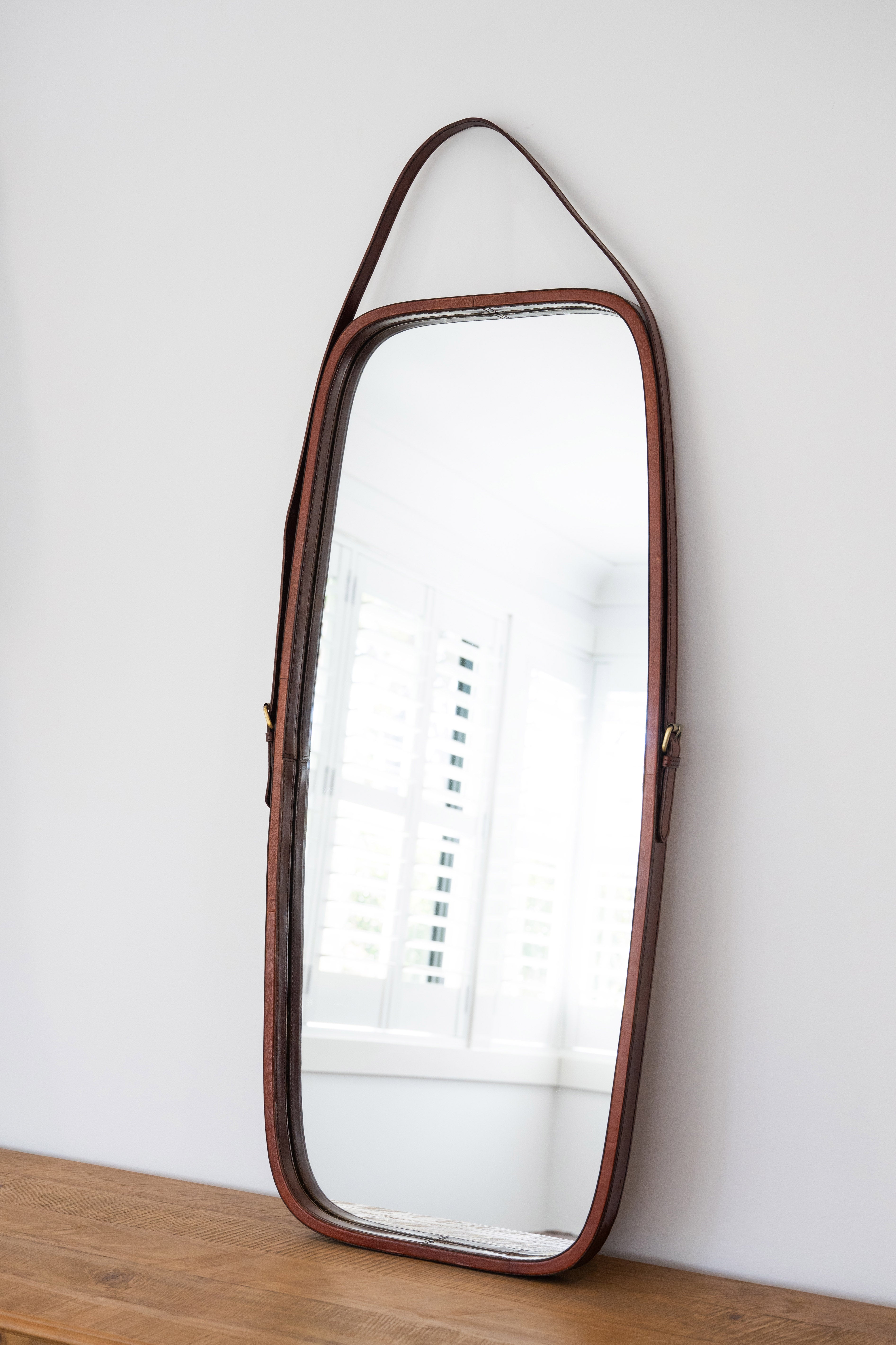 Long rectangular mirror with a brown frame on a wooden surface against a white wall.