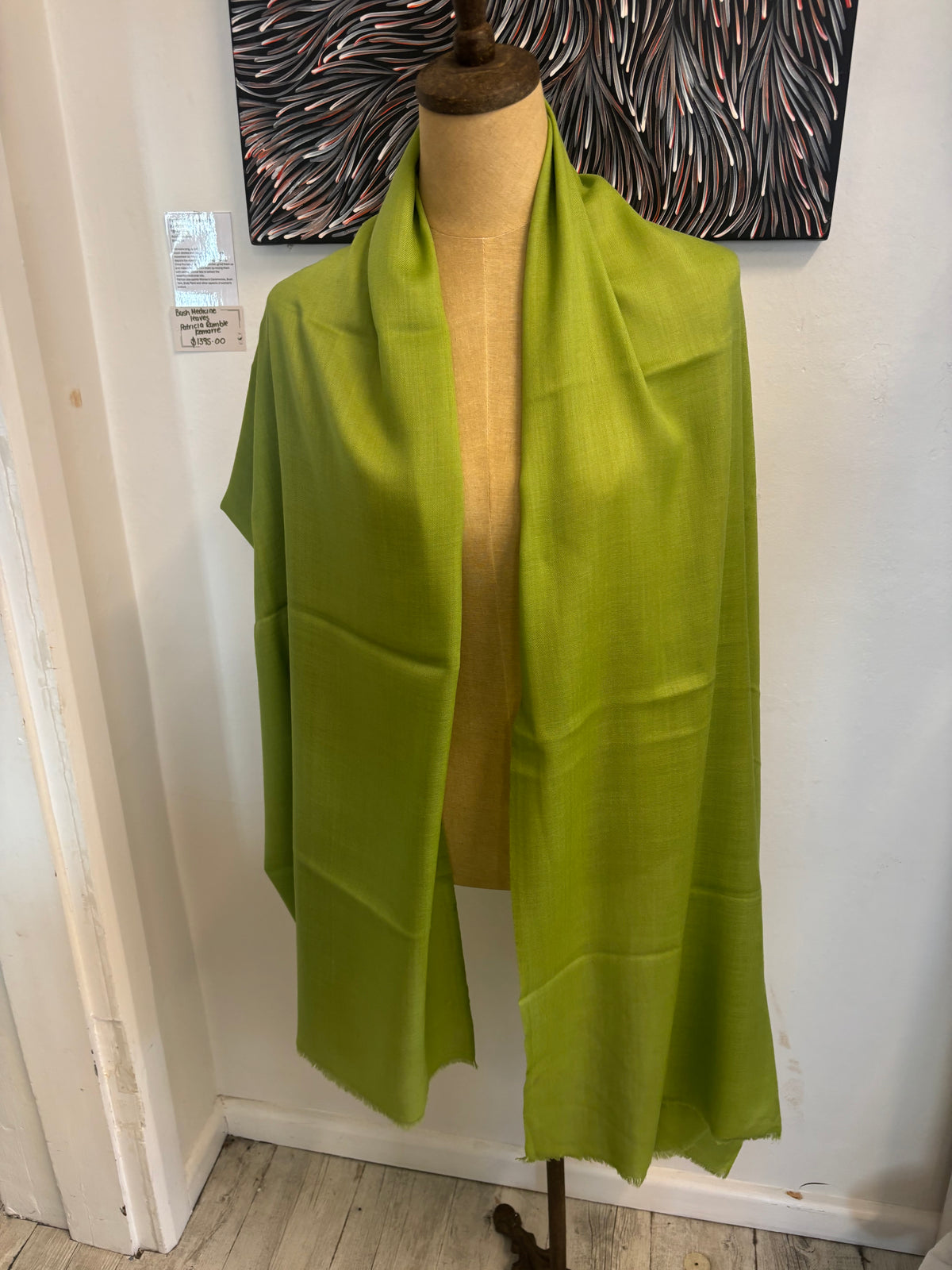Green fabric on a mannequin against a white wall with decorative elements.