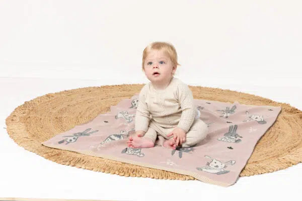 Baby sitting on a pink blanket with animal patterns on a white background