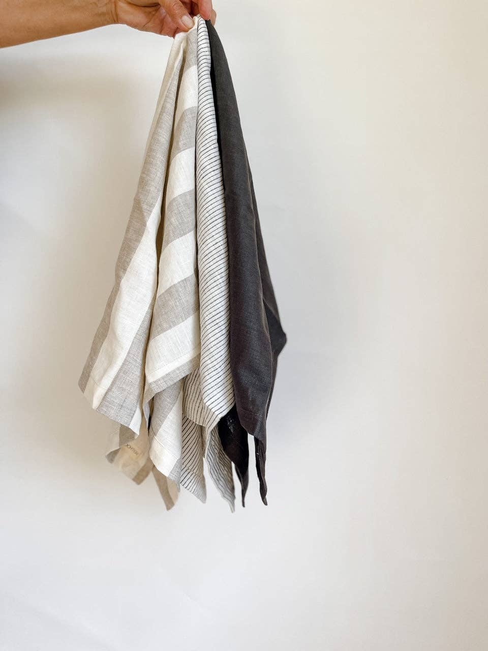 Person holding three folded towels with different patterns against a white background