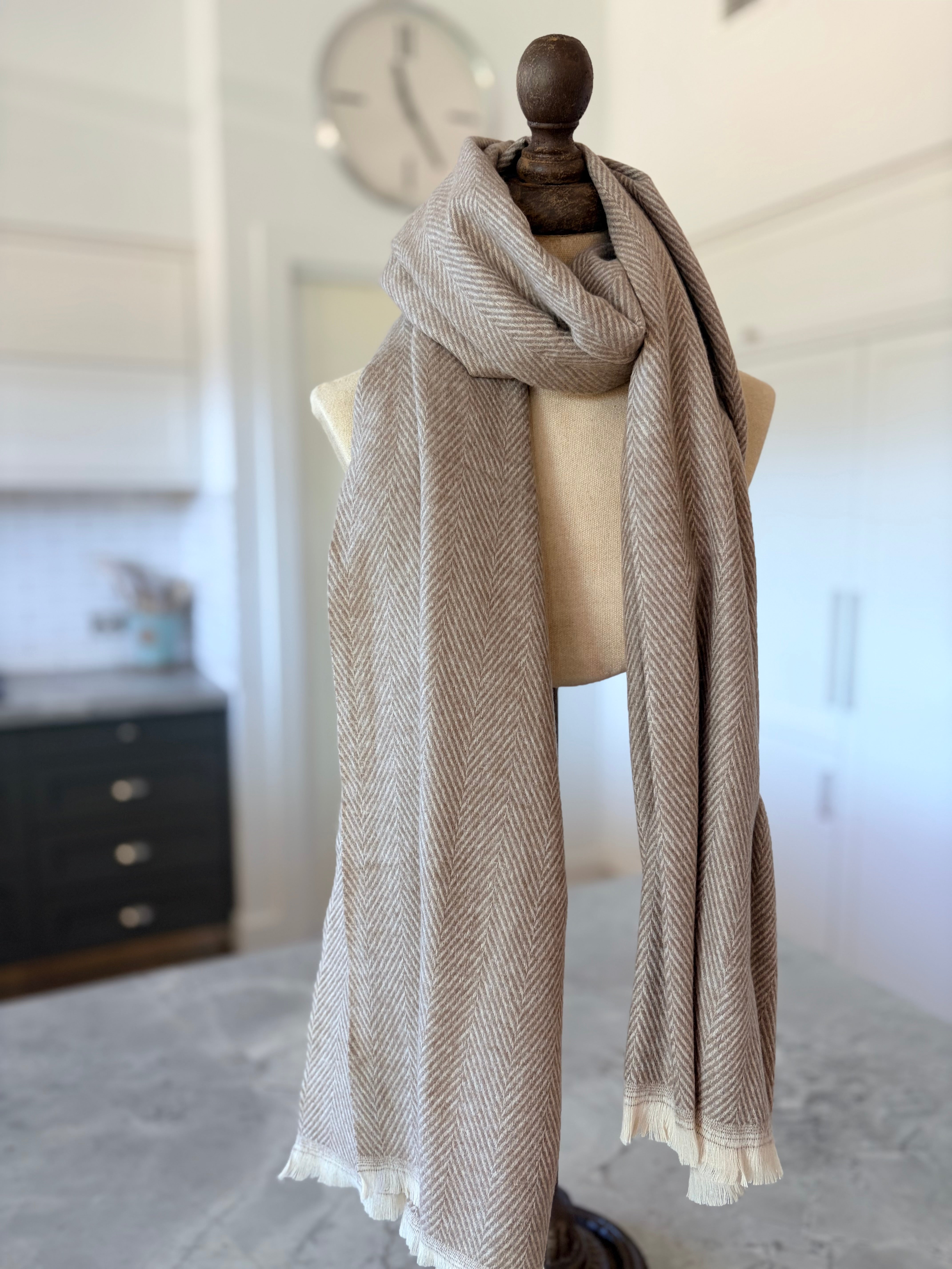 Mannequin wearing a beige scarf in a room with a clock on the wall.