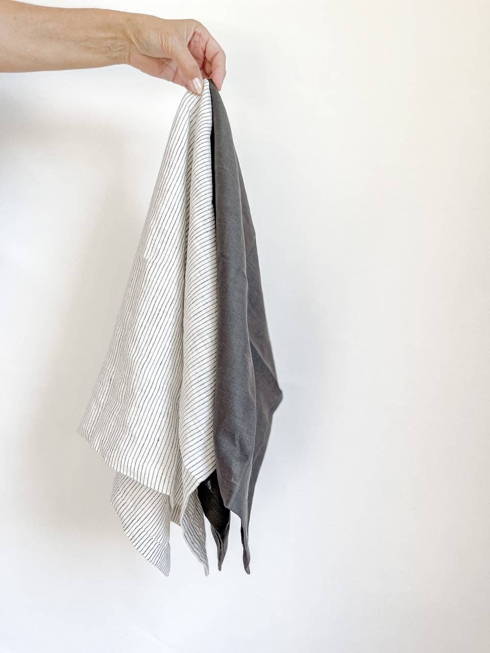 Person holding a folded gray and white towel against a white background