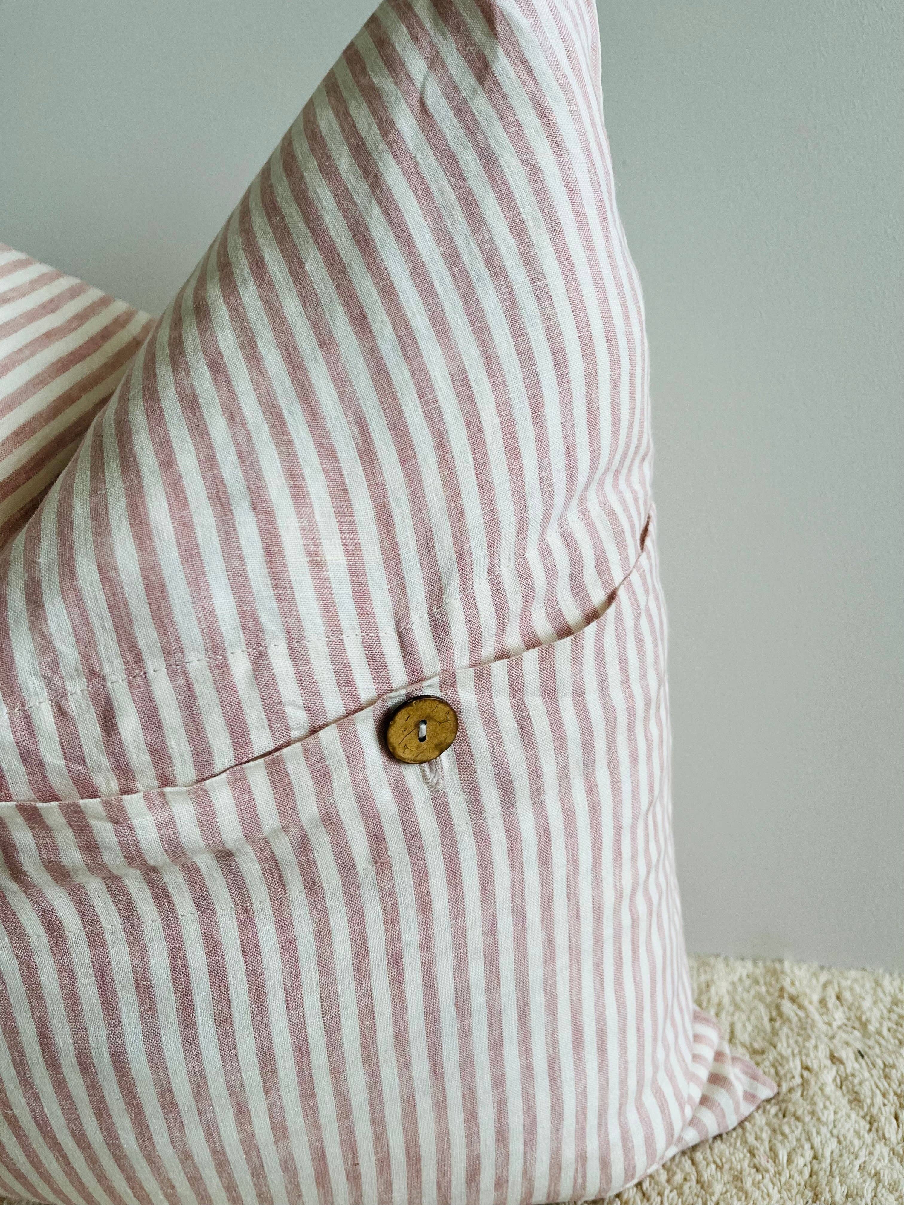 Close-up of a pink and white striped pillow with a button on a neutral background