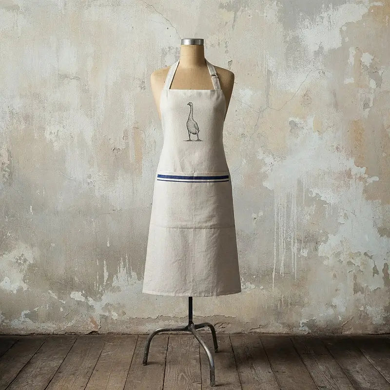 Beige apron with a goose design on a mannequin against a textured wall.