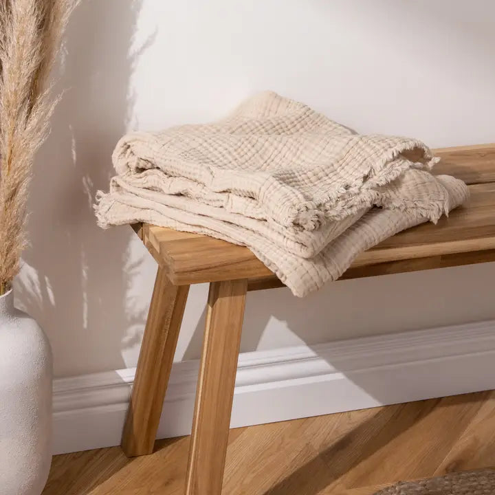 Folded beige textured blanket on a wooden bench against a white wall.