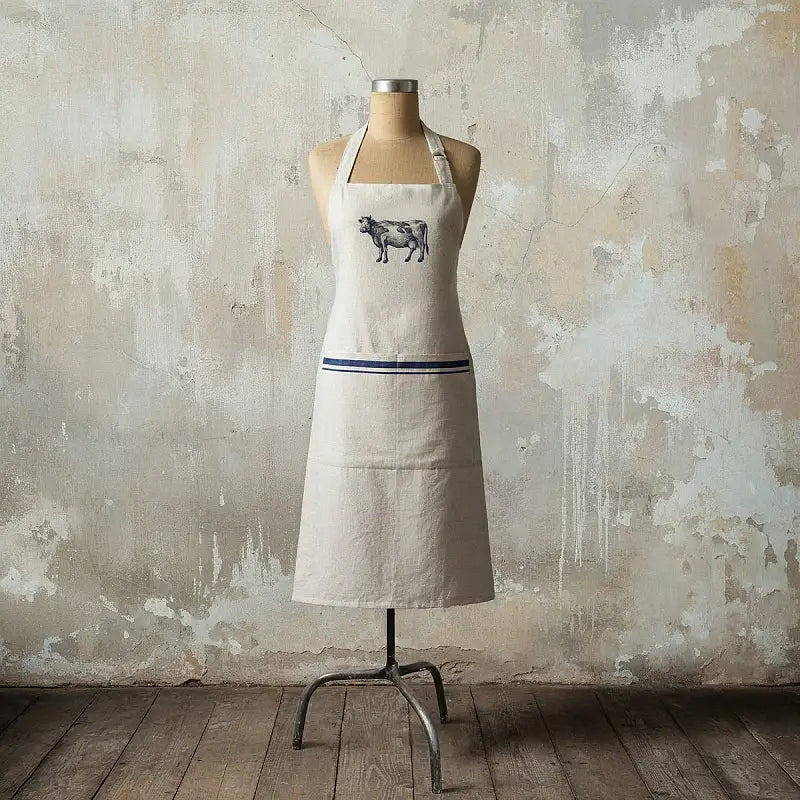 Beige apron with a cow design on a mannequin against a textured wall.