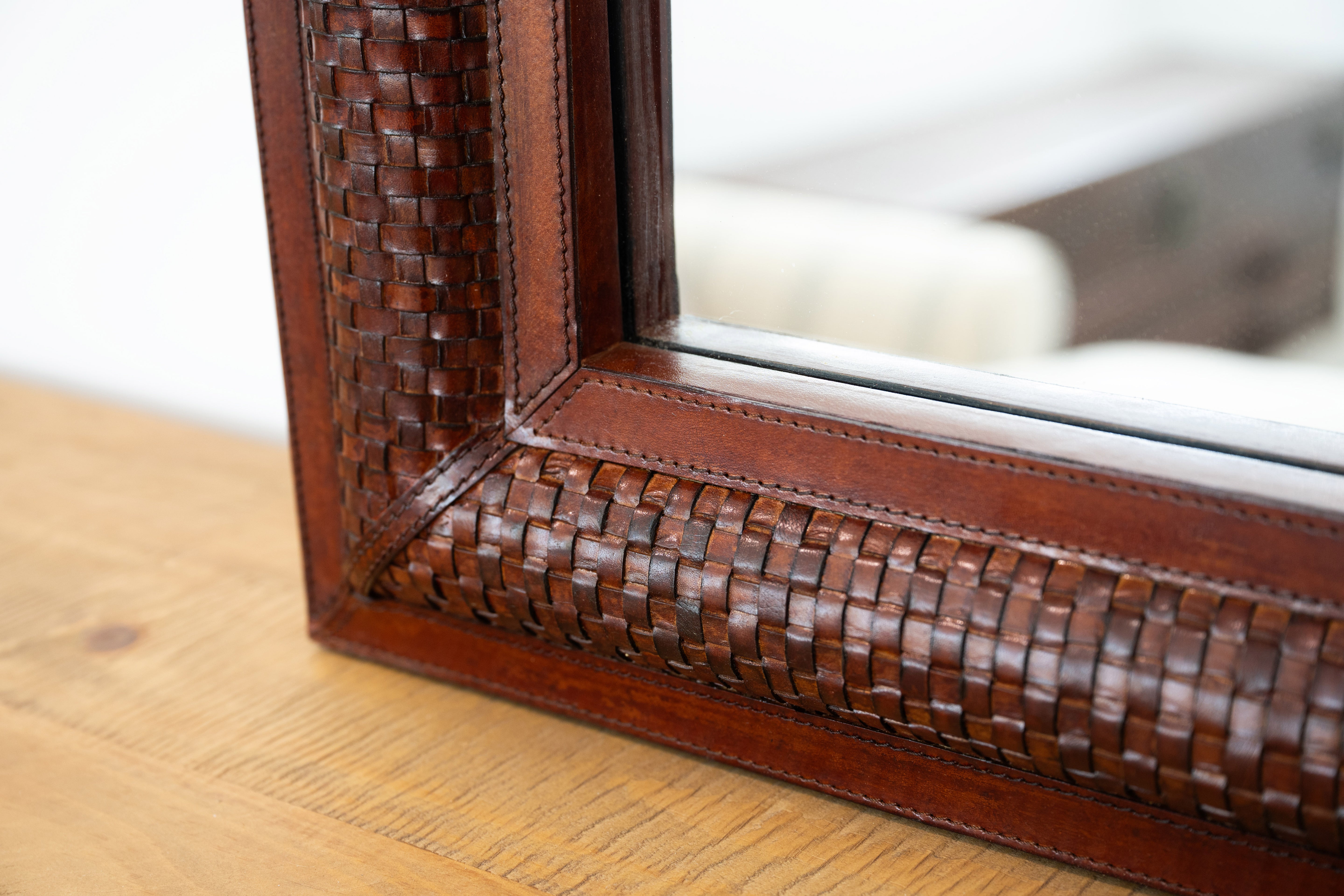 Close-up of a wooden mirror frame with woven detailing on a wooden surface.