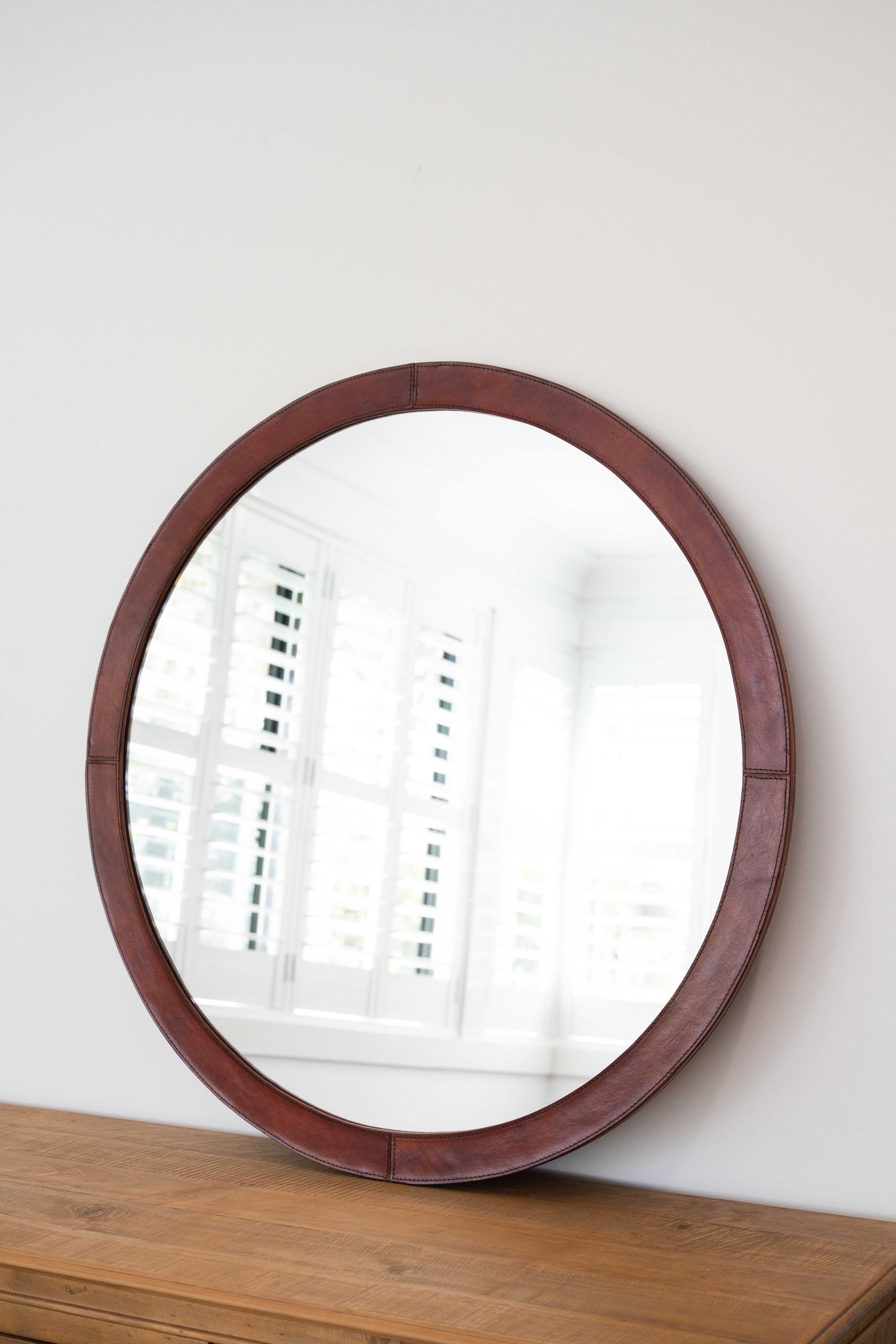 Round wooden-framed mirror on a wooden surface with a white wall background
