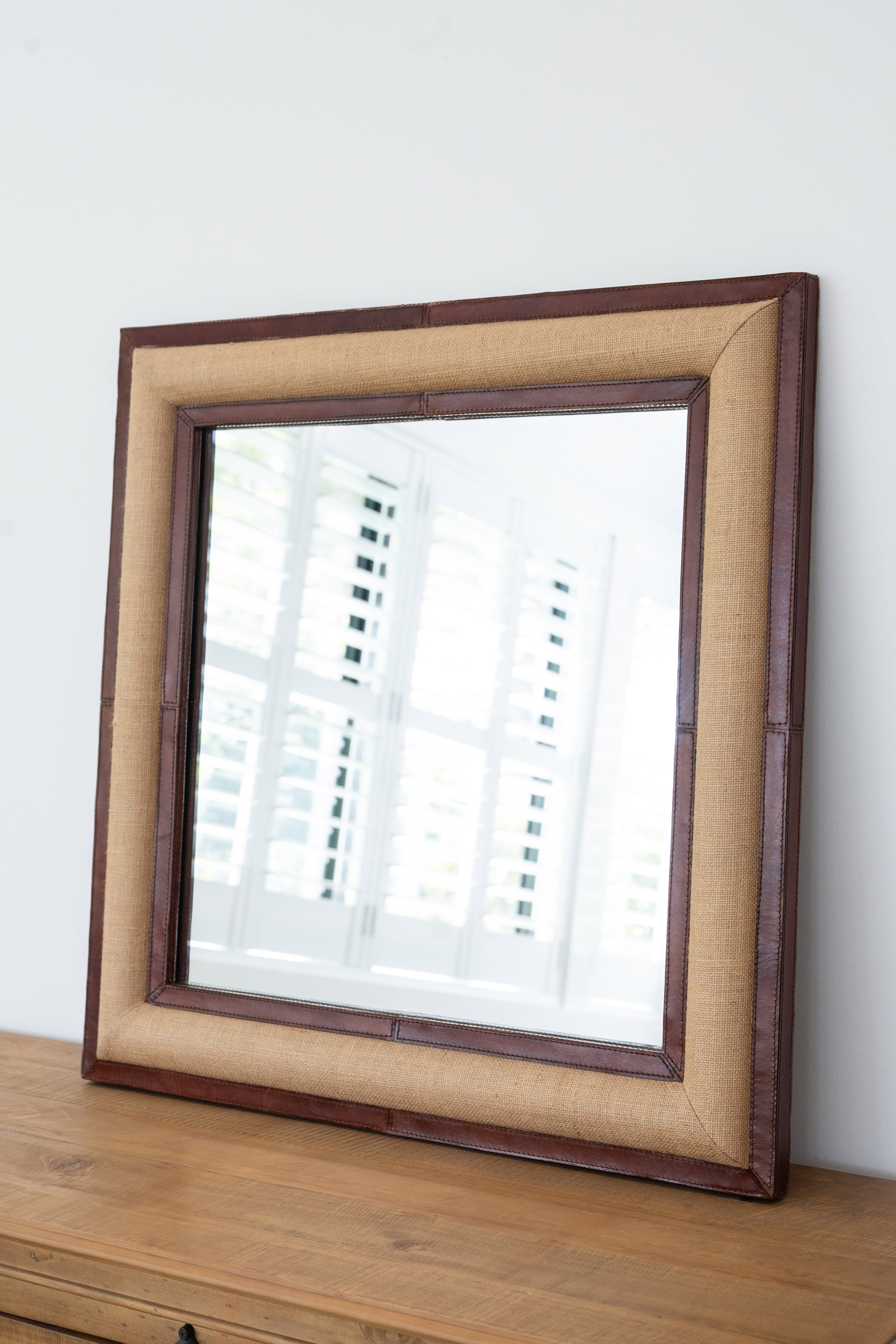 Square mirror with a wooden frame on a wooden surface against a white wall