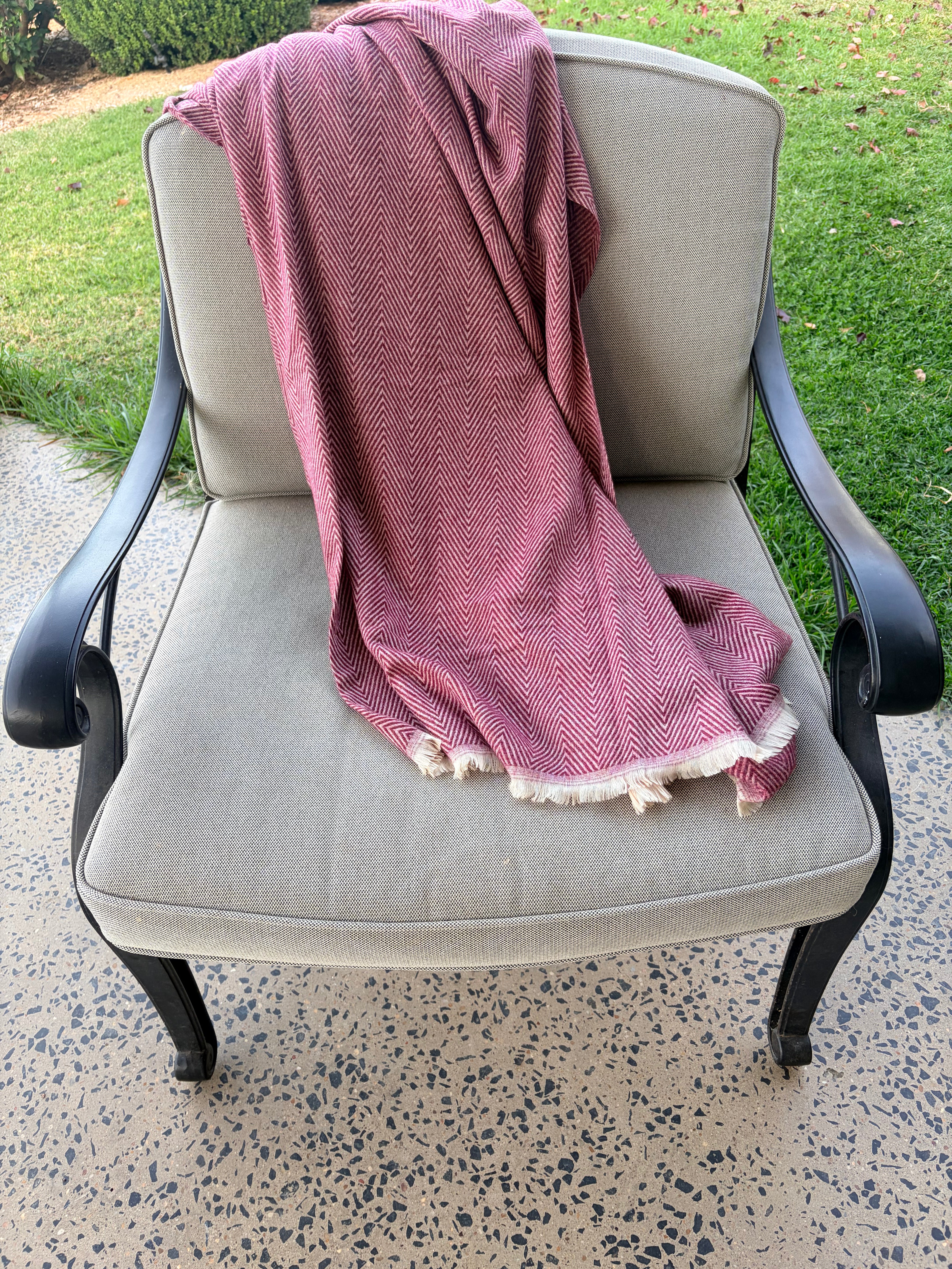 Pink throw draped over a gray chair outdoors on a concrete surface with grass in the background.