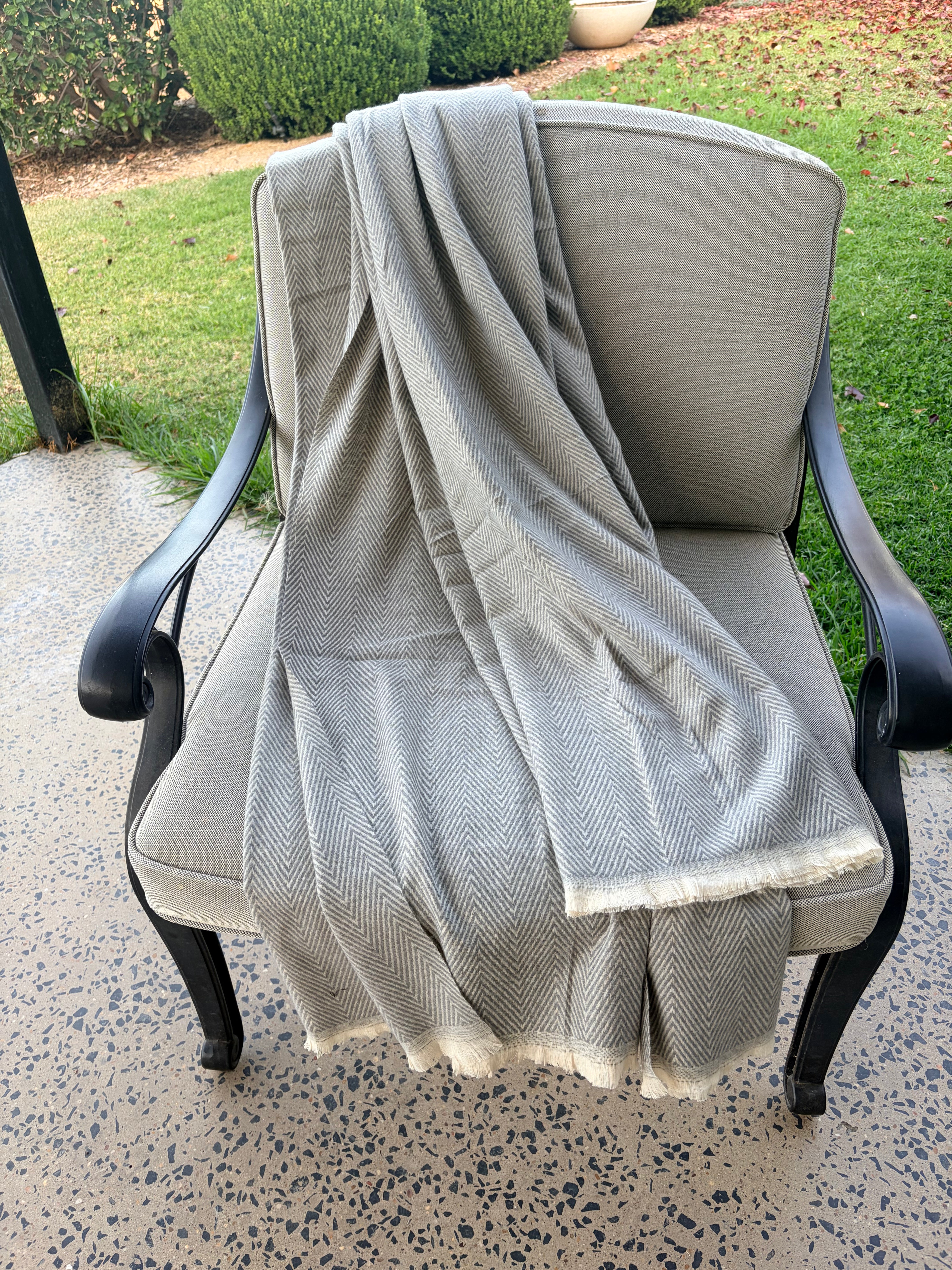 Gray textured throw draped over a chair outdoors on a concrete surface with grass in the background.