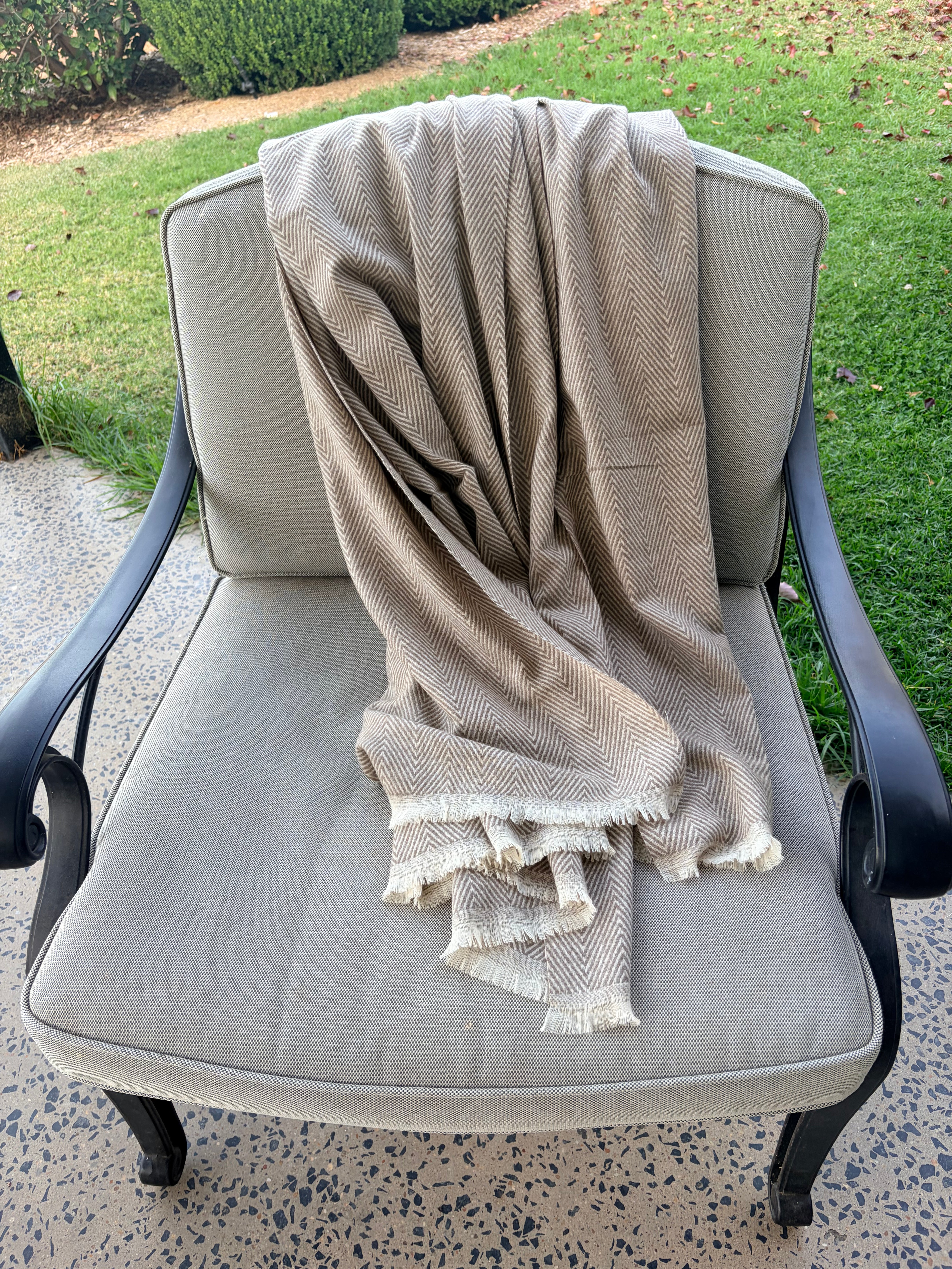 Beige throw draped over a gray chair outdoors on a patio.