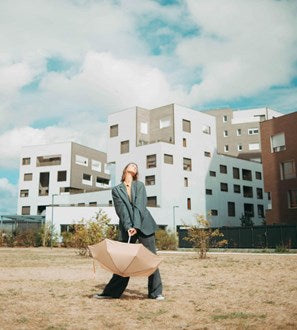 Person holding an umbrella in front of modern apartment buildings under a blue sky with clouds.
