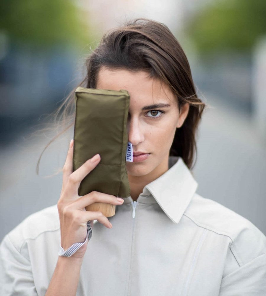 Woman holding a green umbrella against her face outdoors