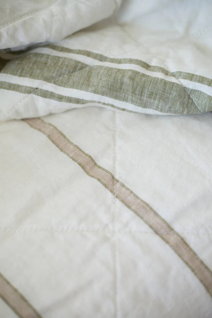 Close-up of a textured white fabric with green and brown stripes on a bed.