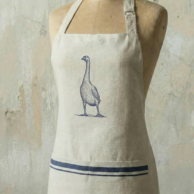 Beige apron with a goose illustration on a wooden mannequin against a textured beige background